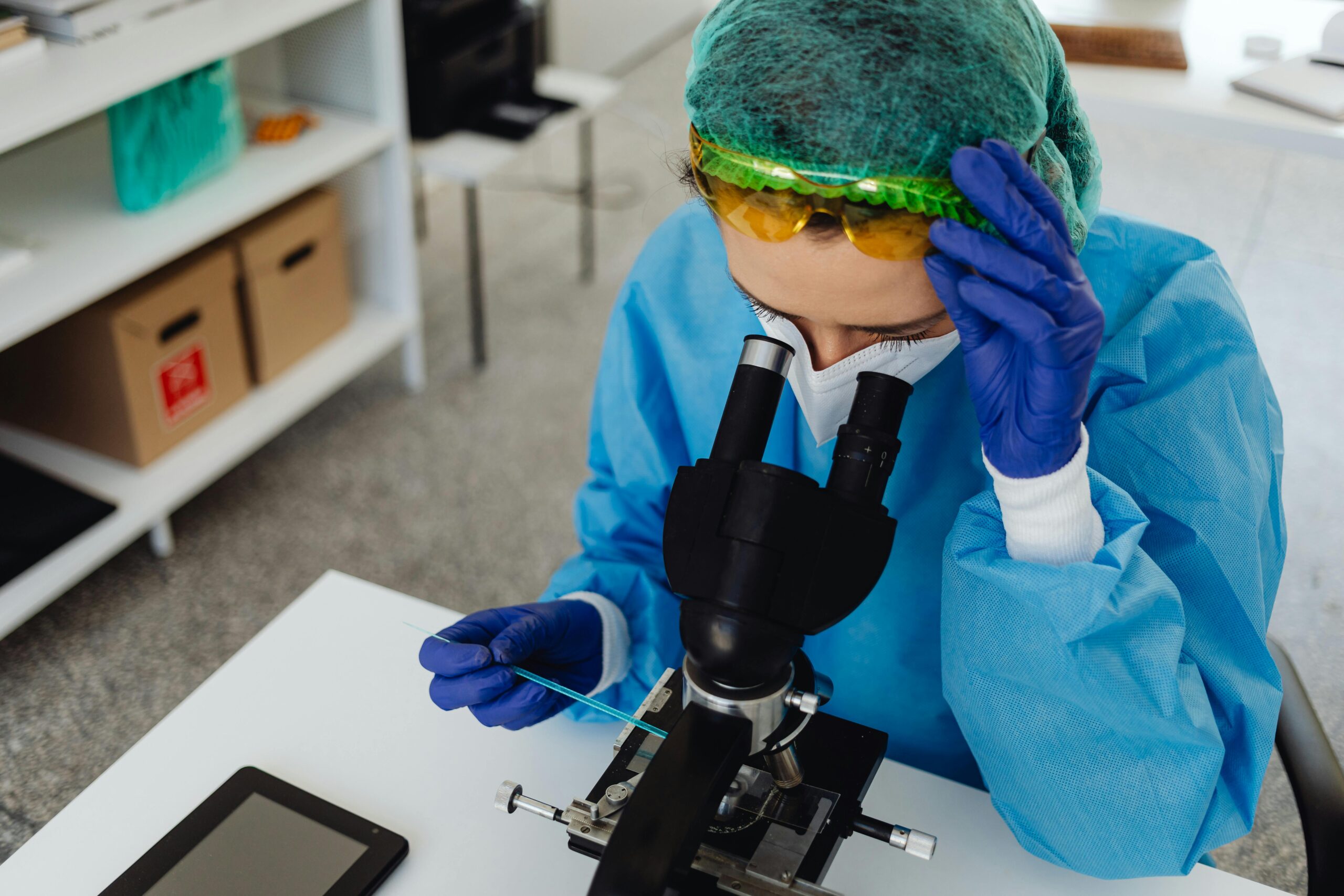 A scientist in protective gear using a microscope for research in a lab setting.