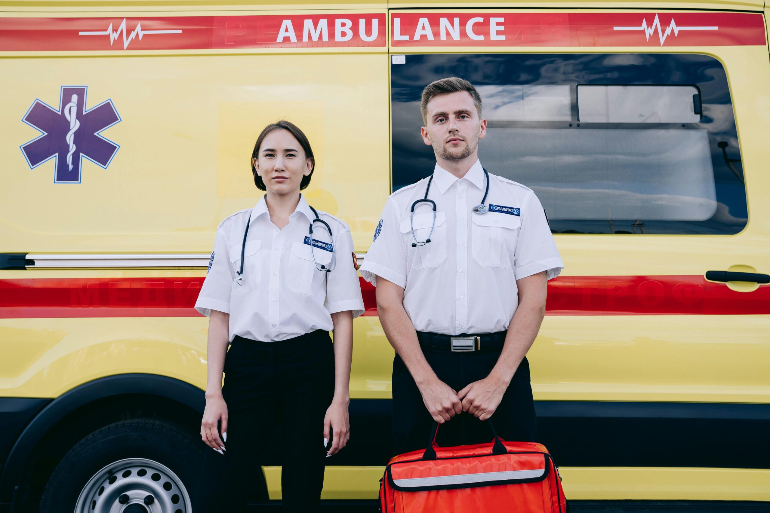 Two paramedics stand confidently in front of a bright yellow ambulance, ready to provide emergency care.