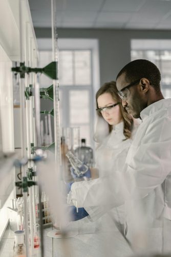 Two scientists in lab coats and safety glasses working in a modern laboratory.